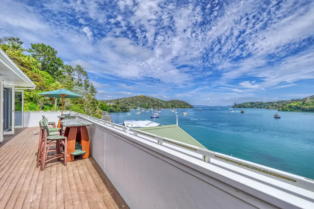 Sunny timber deck with bar seating looking out over a harbour and bush-clad hills